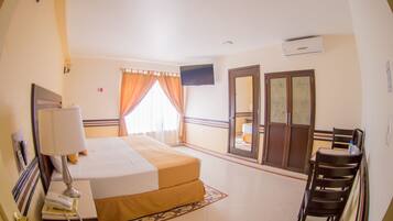 A hotel room with a bed, a desk with a telephone, a chair, a television, and a door leading to a balcony.