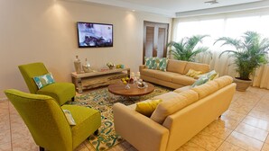 Een woonkamer met een beige bank, een groene fauteuil en een houten salontafel.