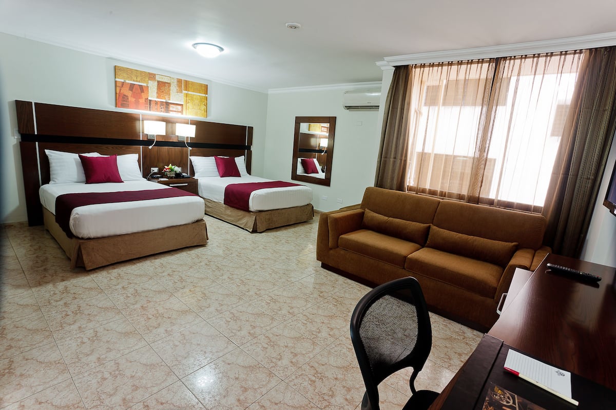 A hotel room with two beds, a sofa, a desk, and a chair.