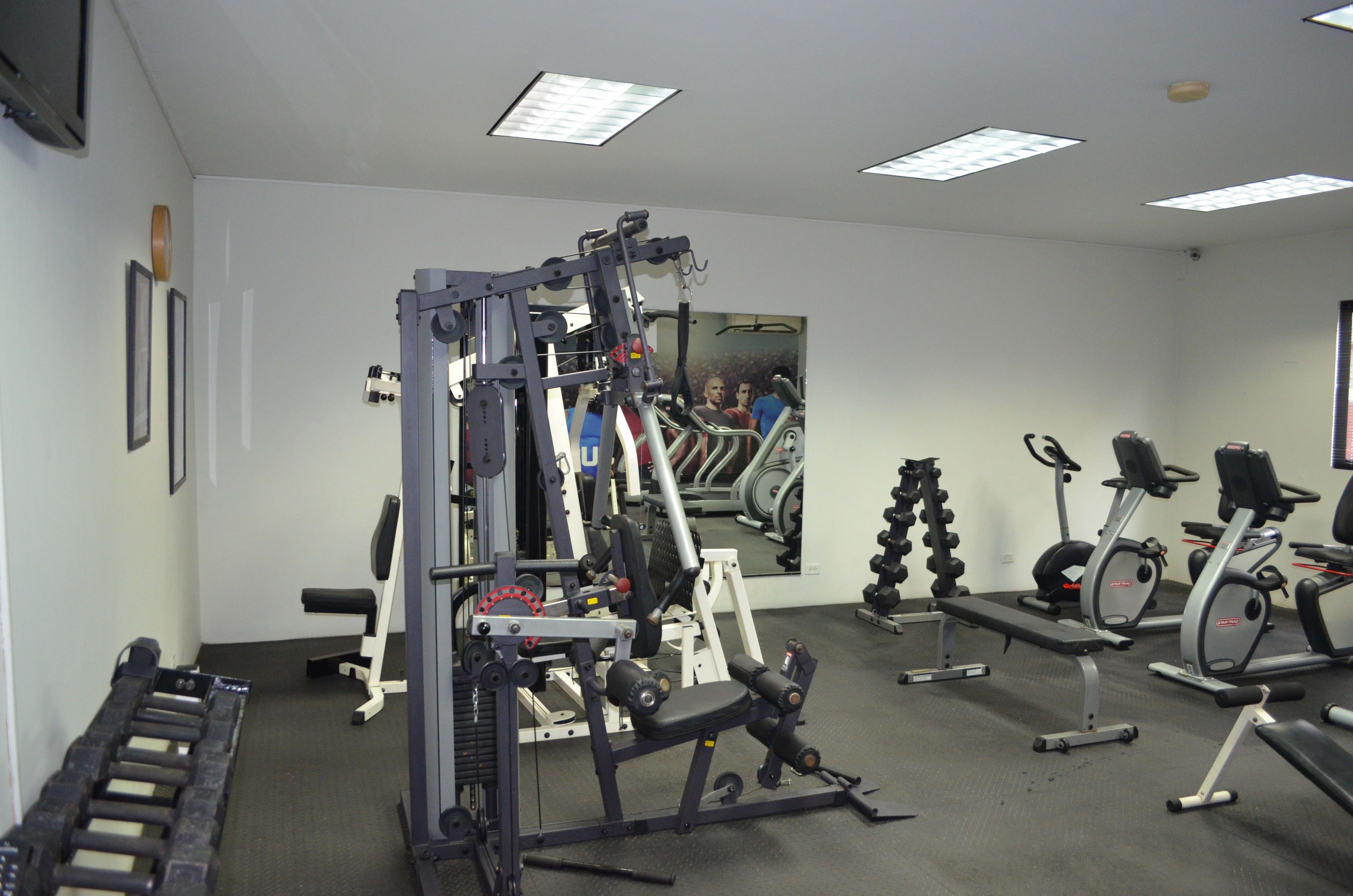 A gym with various exercise equipment, including a weight bench, dumbbells, and a treadmill.
