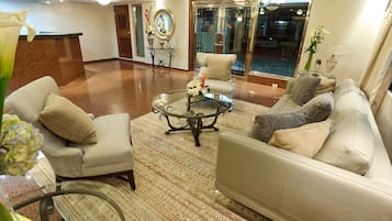 A spacious lobby with a reception desk, seating area with sofas and armchairs, a patterned carpet, and a large mirror.