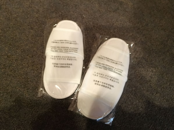 Dos pantuflas blancas en empaque de plástico sobre una superficie oscura.