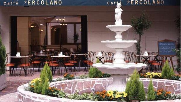 A fountain in a stone basin surrounded by chairs and tables, with a cafe named 'ERCOLANO' in the background. - Hotel Yokohama Camelot Japan (Yokohama)