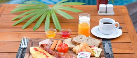 A breakfast table with eggs, bacon, toast, bread, butter, cheese, and a cup of coffee.