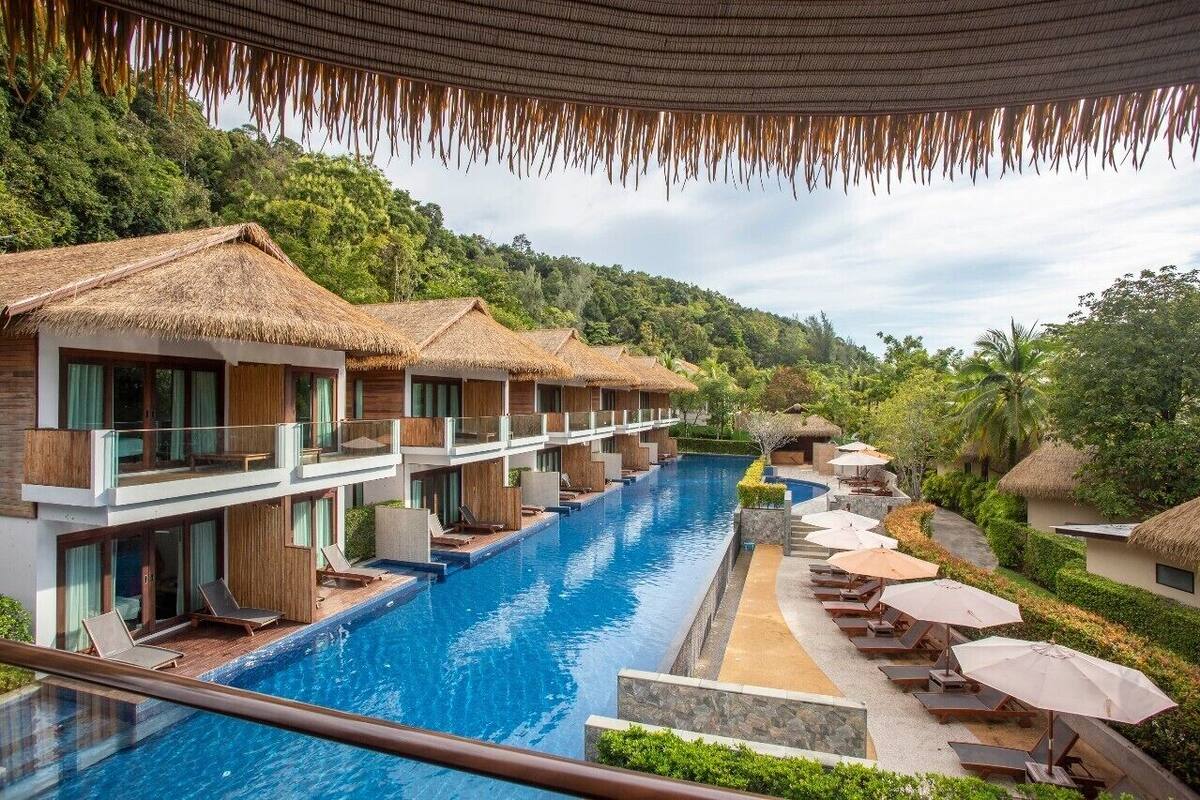 A resort with a swimming pool, thatched-roof bungalows, and lush greenery.