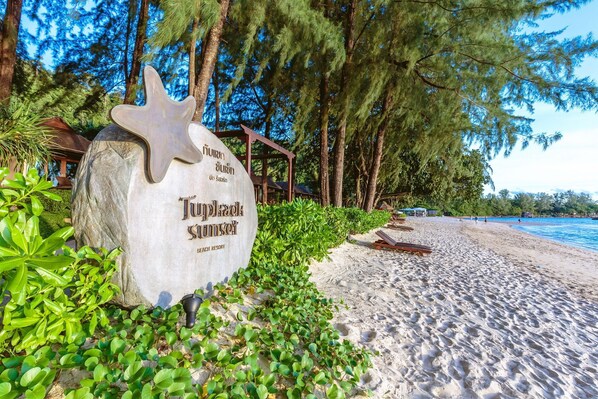 A stone sign with the text "Tropical Sunset Beach Resort" surrounded by greenery and a sandy beach. - Tup Kaek Sunset Beach Resort (Krabi)
