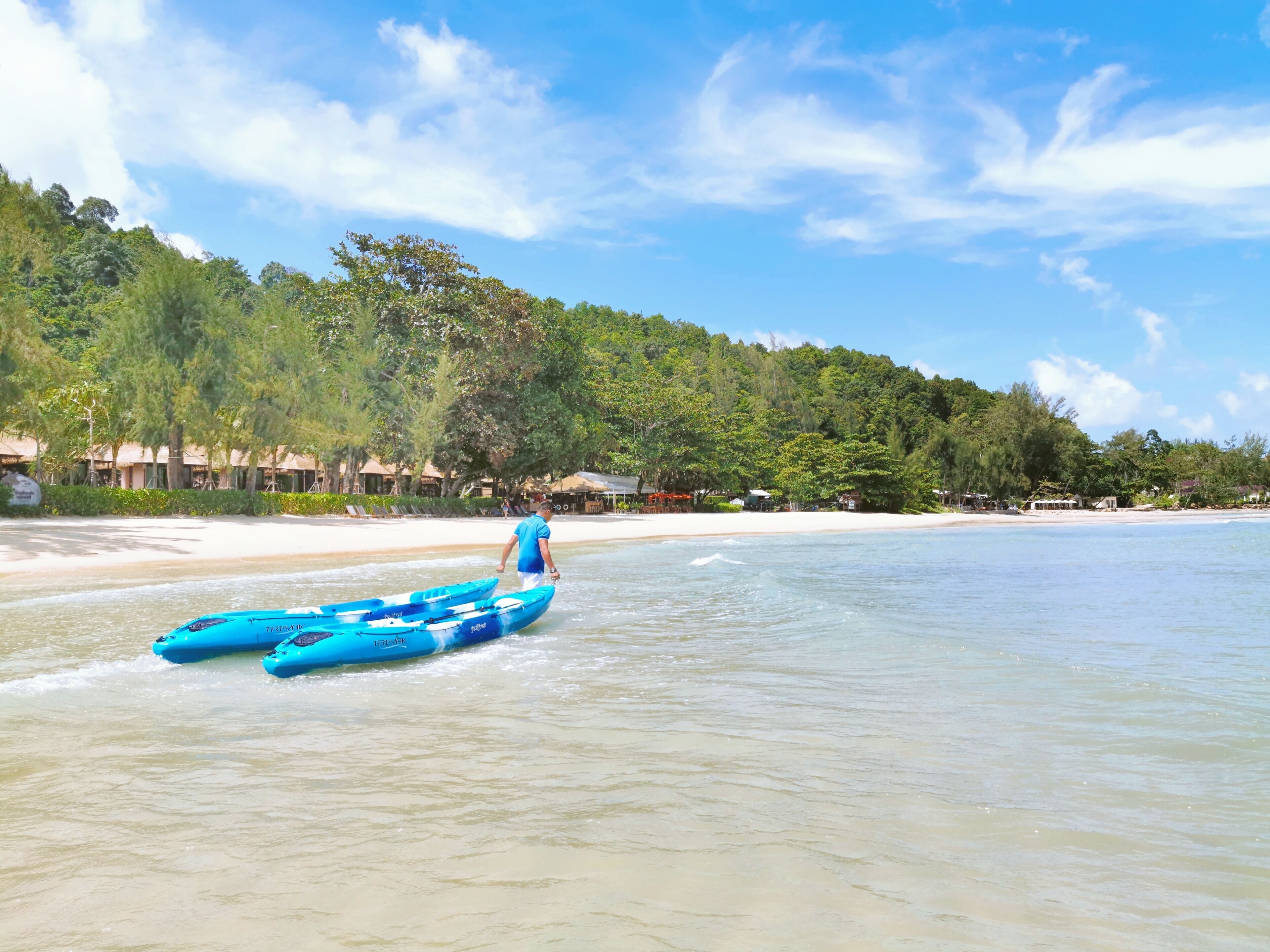 A beach with two blue kayaks, a sandy shore, and a forested hill in the background.