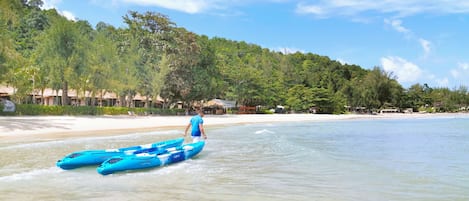 A beach with two blue kayaks, a sandy shore, and a forested hill in the background.