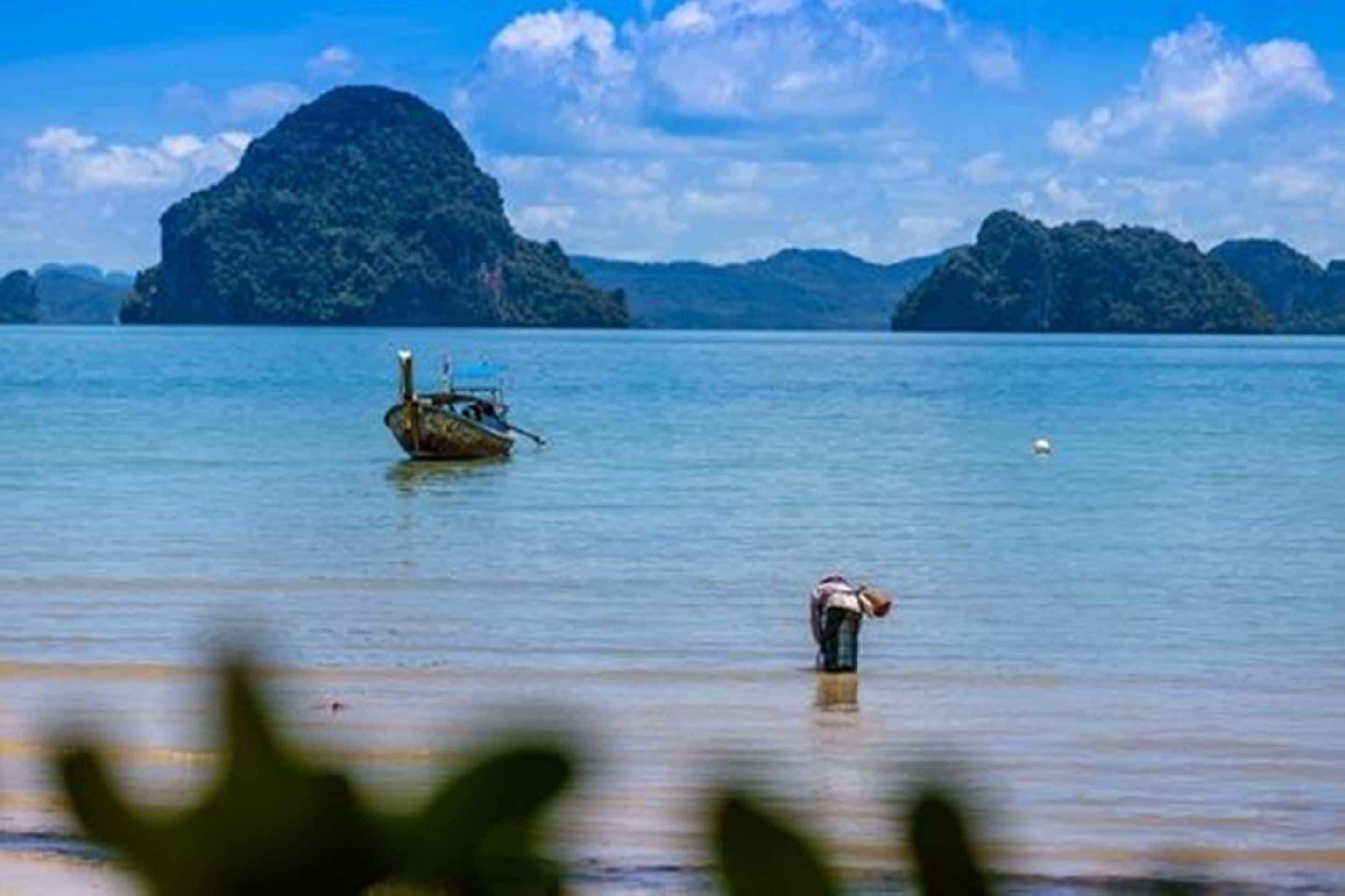 A calm sea with a boat and a person standing in shallow water.