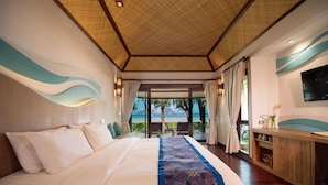 Habitación de hotel con una cama grande, un televisor montado en la pared y vista a la playa por la ventana.