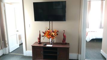 A hotel room with a flat-screen TV mounted on a wooden console, a vase with autumn flowers, and a bed with a white comforter.
