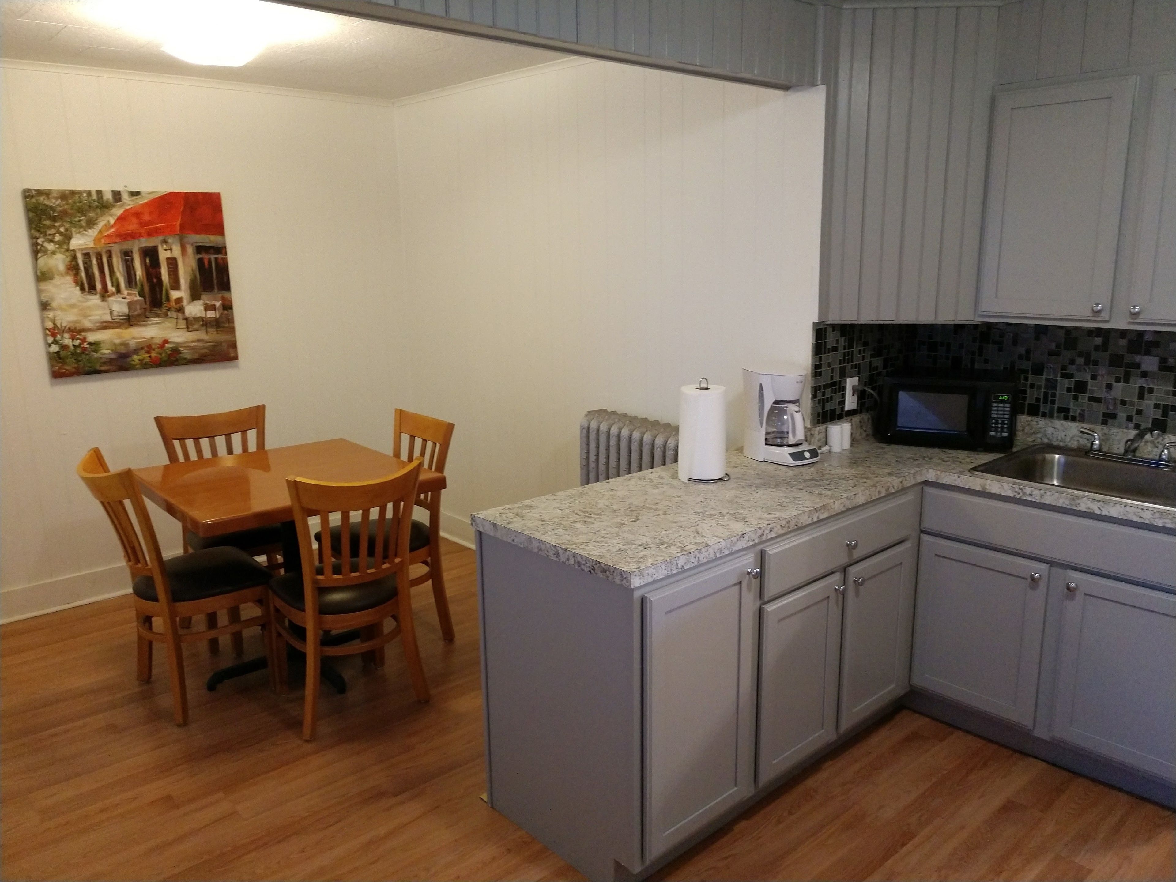 A compact kitchen with a dining table and chairs, a coffee maker, a microwave, and a sink.