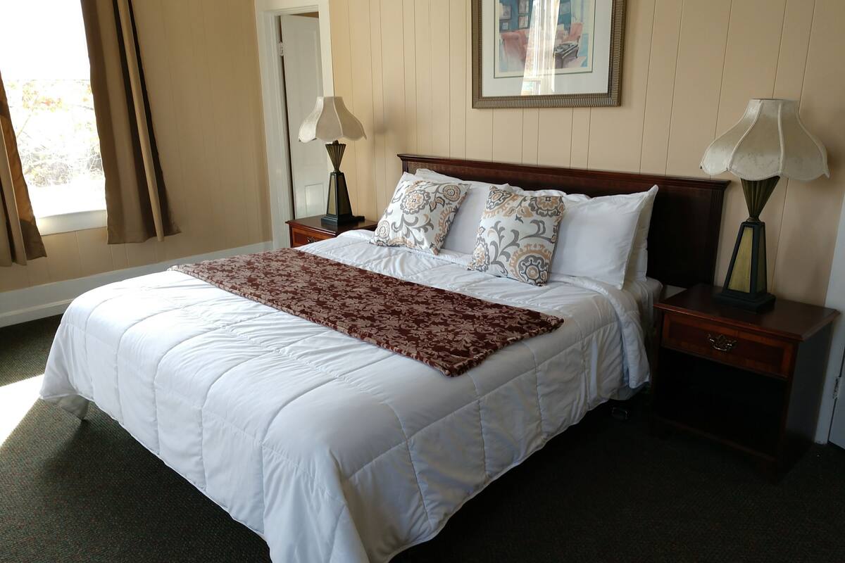 A neatly made bed with a patterned throw, two bedside lamps, and a framed picture on the wall.