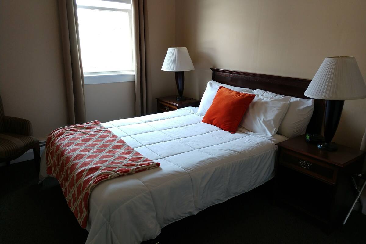 A hotel room with a large bed, two bedside tables with lamps, a chair, and a window with curtains.
