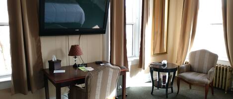 Une chambre d’hôtel équipée d’une télévision, d’un bureau avec une lampe, d’une chaise, d’une petite table et d’un radiateur.