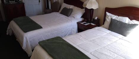 Une chambre d’hôtel avec deux lits, chacun recouvert d’un plaid vert, une table de chevet avec une lampe et un tableau encadré au mur.