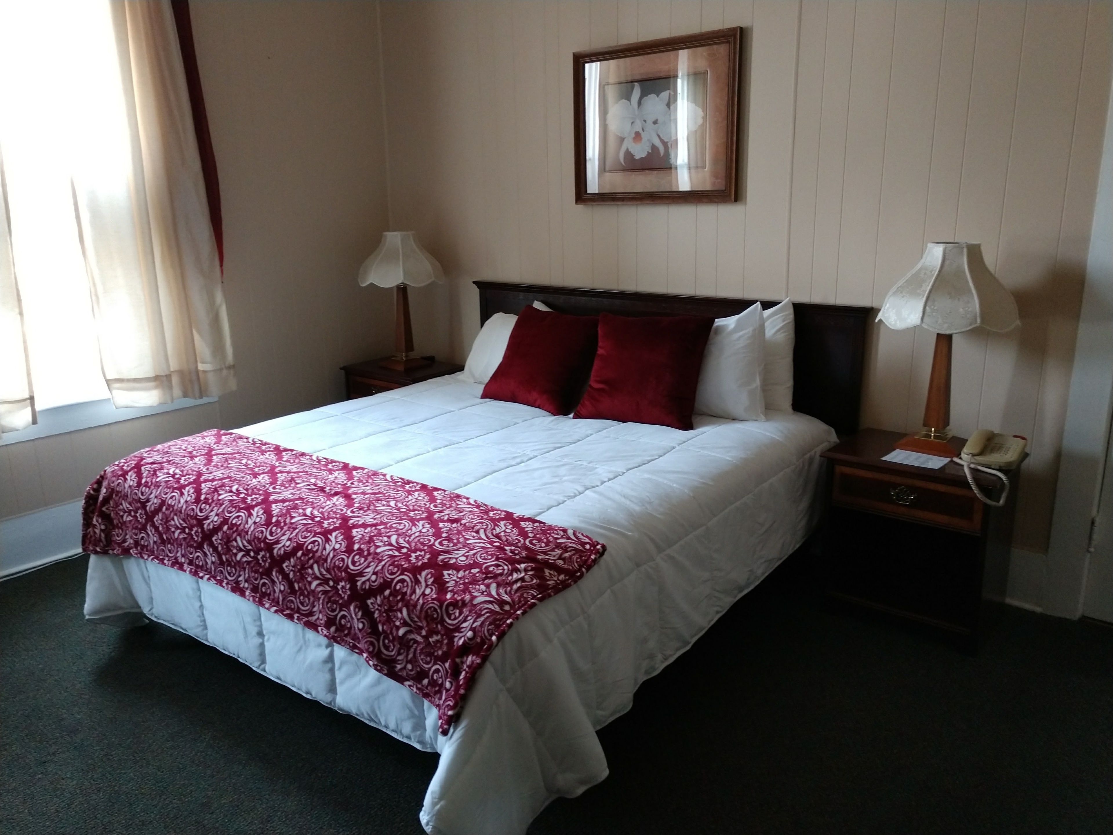 Habitación de hotel con una cama grande, dos mesitas de noche con lámparas, un cuadro enmarcado en la pared y una ventana con cortinas.