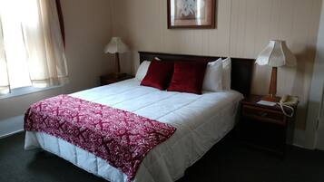 Habitación de hotel con una cama grande, dos mesitas de noche con lámparas, un cuadro enmarcado en la pared y una ventana con cortinas.
