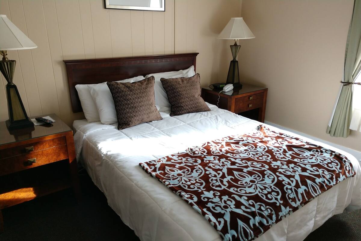 A neatly made bed with a patterned throw blanket, a wooden headboard, and two bedside tables with lamps.