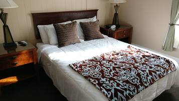 Una cama bien tendida con un plaid estampado, un cabecero de madera y dos mesitas de noche con lámparas.