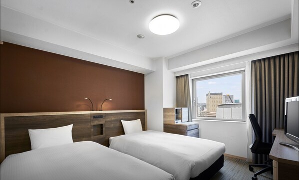 Une chambre d’hôtel avec deux lits, un bureau, une chaise, une fenêtre avec des rideaux et une vue sur la ville.
