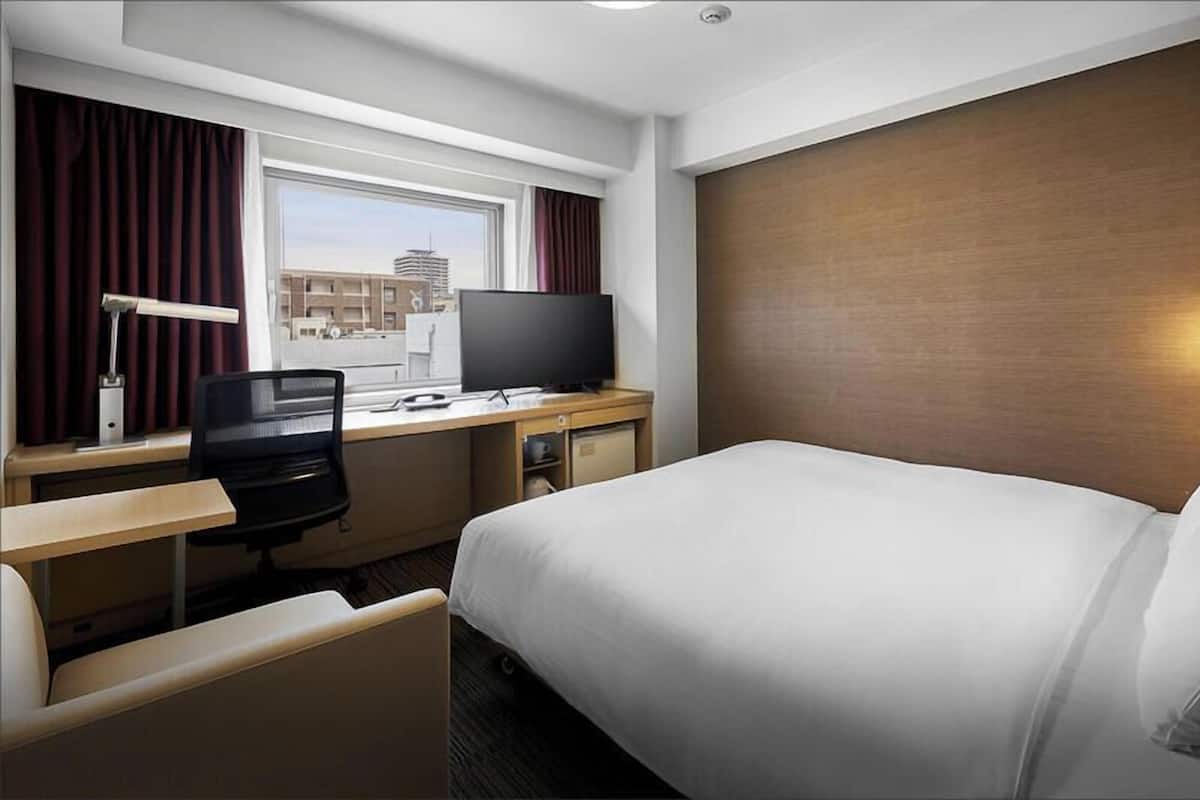 Une chambre d’hôtel avec un lit, un bureau, une chaise, une télévision et une fenêtre avec des rideaux.
