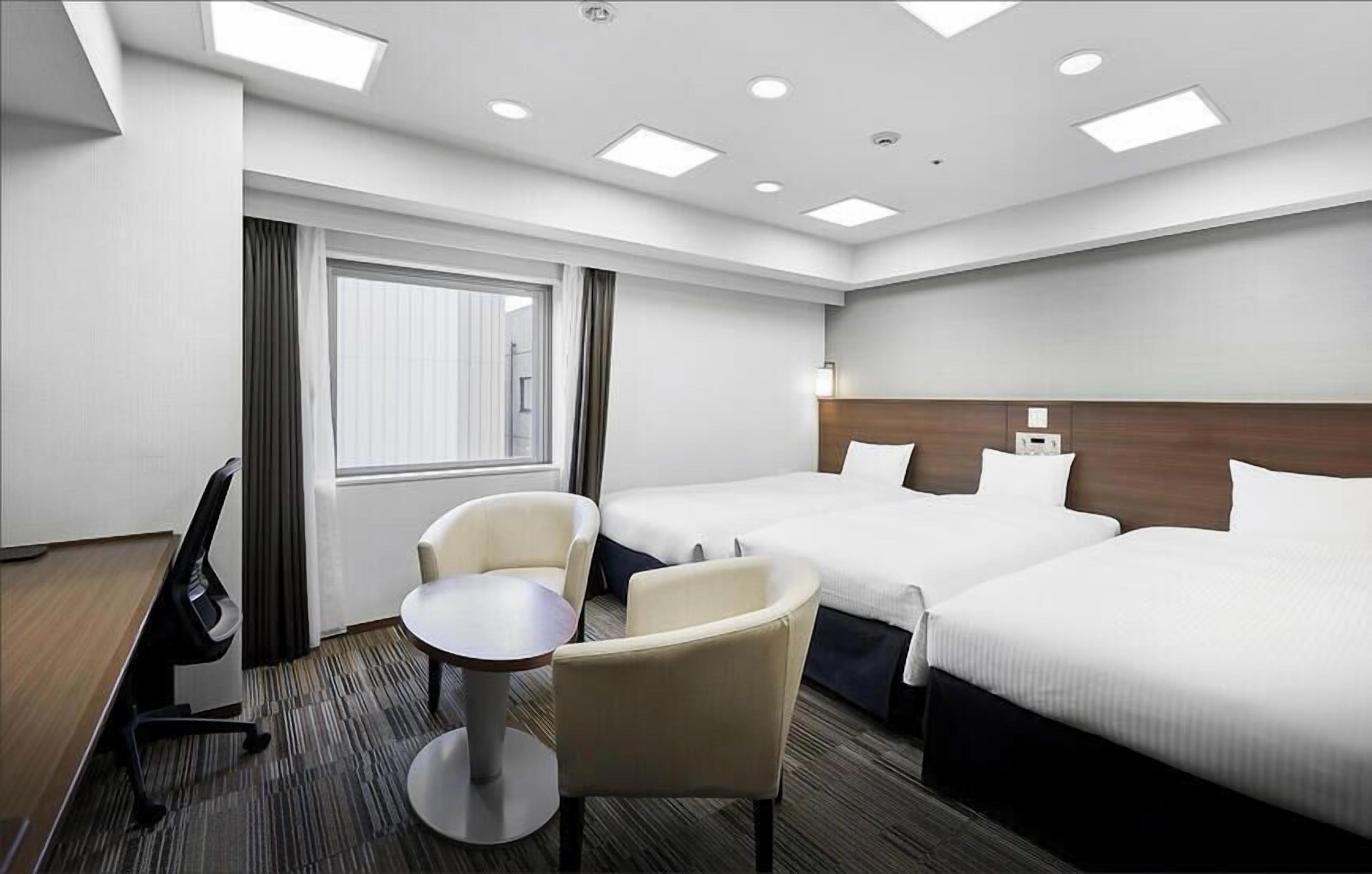A hotel room with two beds, a desk, a chair, and a window with curtains.