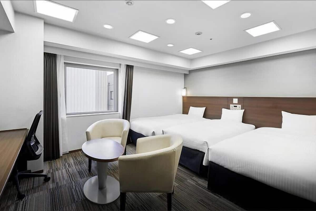 Une chambre d’hôtel avec deux lits, un bureau, une chaise et une fenêtre avec des rideaux.