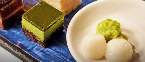 A dessert plate with various sweets, including a green square and two white round items, on a blue cloth.