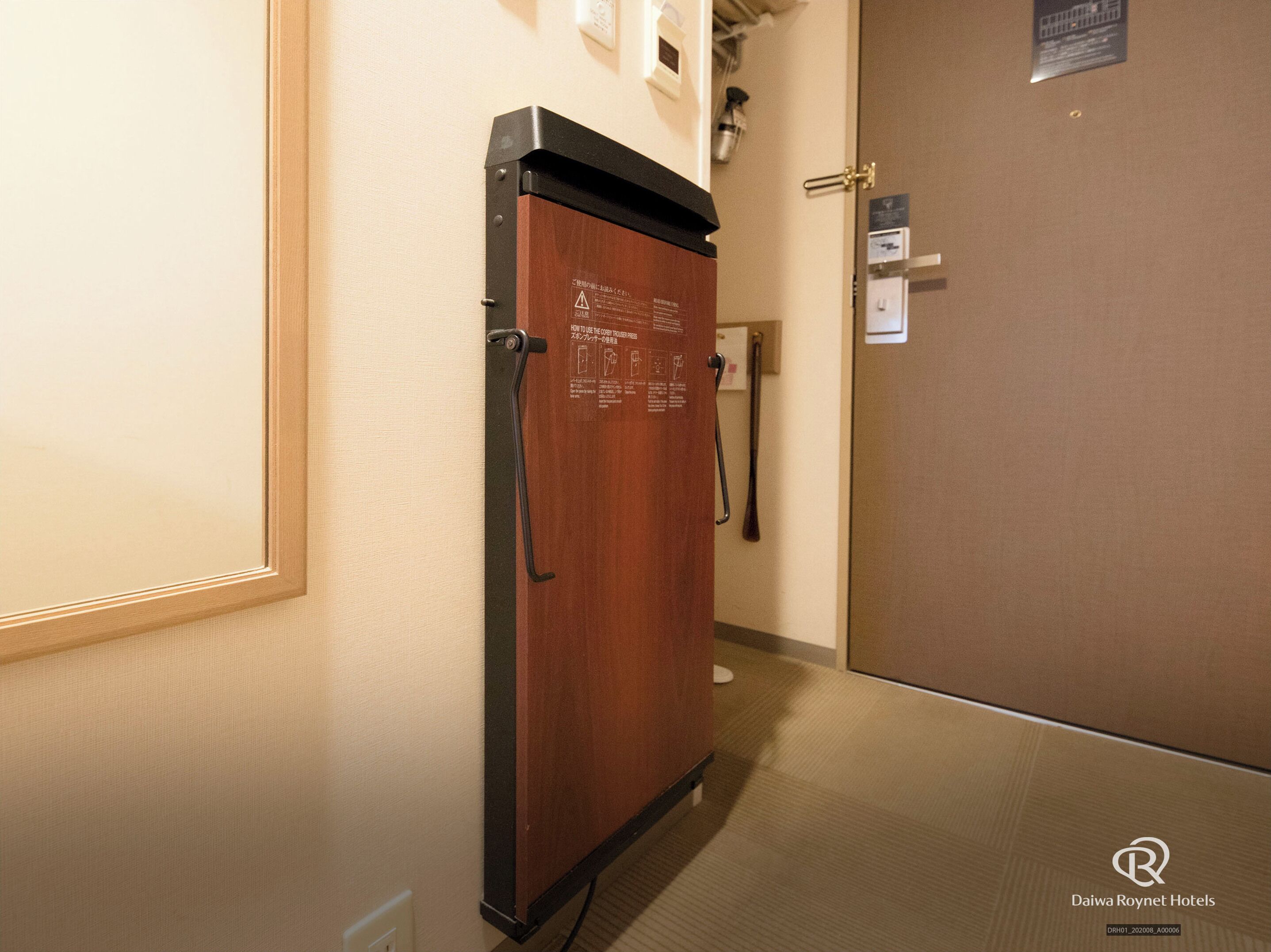 Un pasillo con una puerta de madera y un picaporte de metal, un cartel en la pared, y una puerta con lector de tarjeta de acceso.
