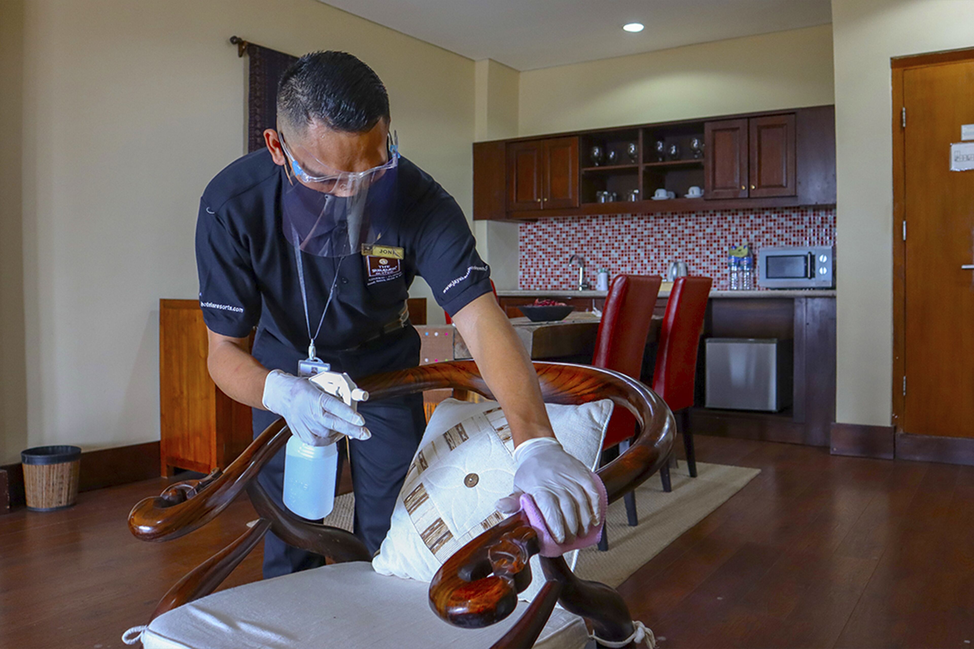 A person cleaning a wooden chair in a room with a kitchen in the background.