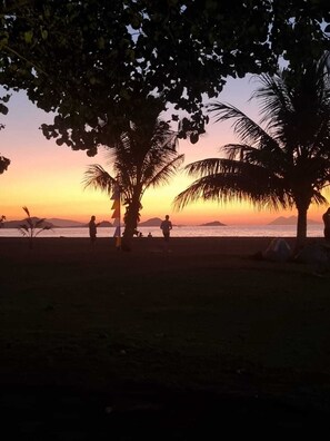 Une scène de plage avec des palmiers et des personnes se promenant le long du rivage au coucher du soleil.