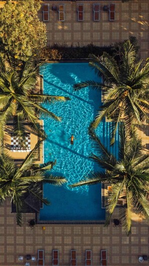 An aerial view of a rectangular swimming pool surrounded by palm trees, with a person swimming in the center. - The Jayakarta Suite Komodo Flores (Labuan Bajo)