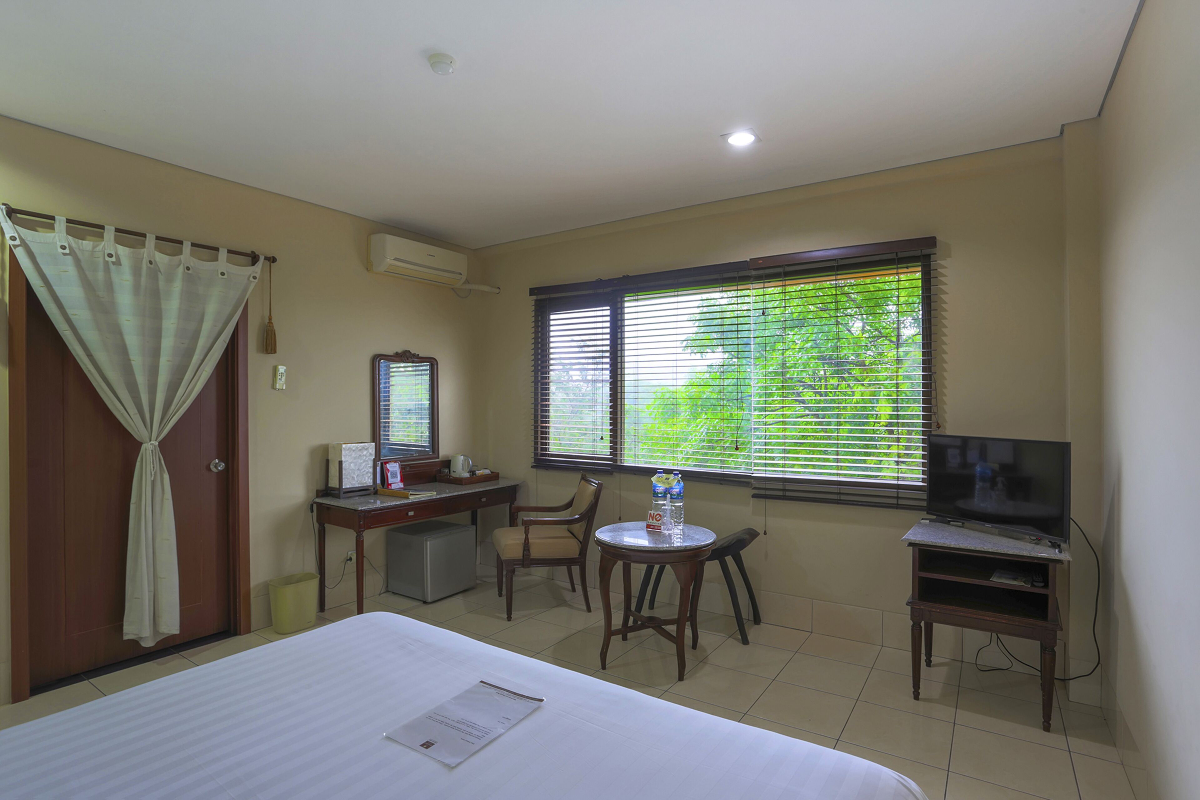 A hotel room with a bed, a desk with a computer, a TV, and a window with blinds.