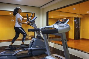 Une femme fait de l’exercice sur un tapis de course dans une salle de sport, avec un mur recouvert de miroirs et une fenêtre bien visible.