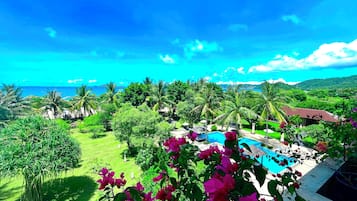 Relax by the serene pool surrounded by lush greenery and palm trees, with breathtaking views of the ocean and mountains.