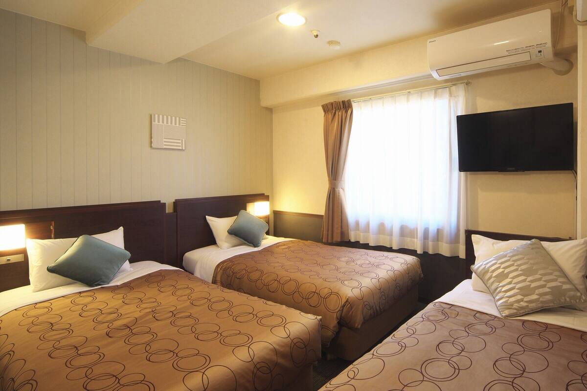 Ein Hotelzimmer mit zwei Betten, einem Flachbildfernseher, einer Klimaanlage und einem Fenster mit Vorhängen.