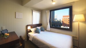 A hotel room with a bed, a desk with a laptop, a chair, a lamp, and a window with a city view. - Yokohama Heiwa Plaza Hotel (Yokohama)