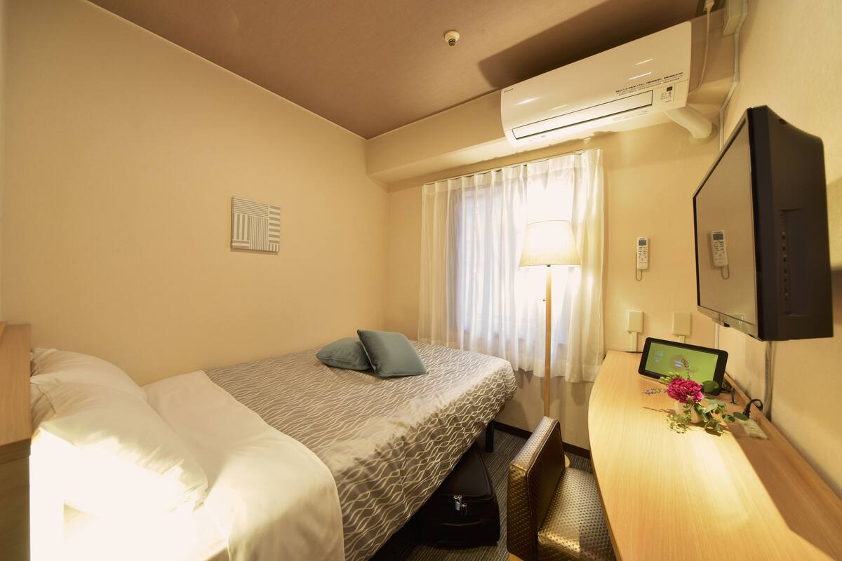Ein Hotelzimmer mit Bett, Schreibtisch mit Computer, Fernseher und Klimaanlage.