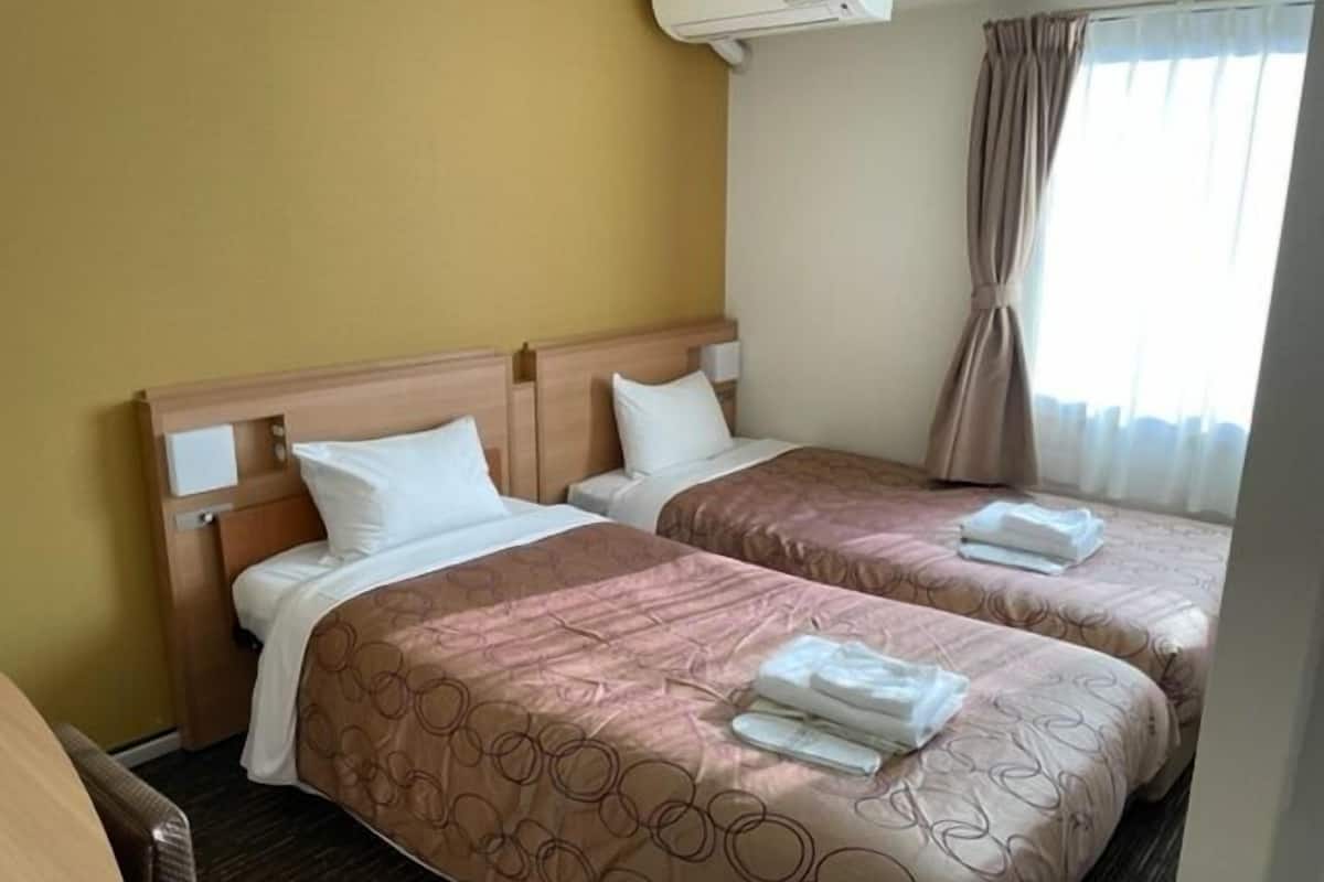 Una habitación de hotel con dos camas, un cabecero de madera, una ventana con cortinas y un equipo de aire acondicionado.