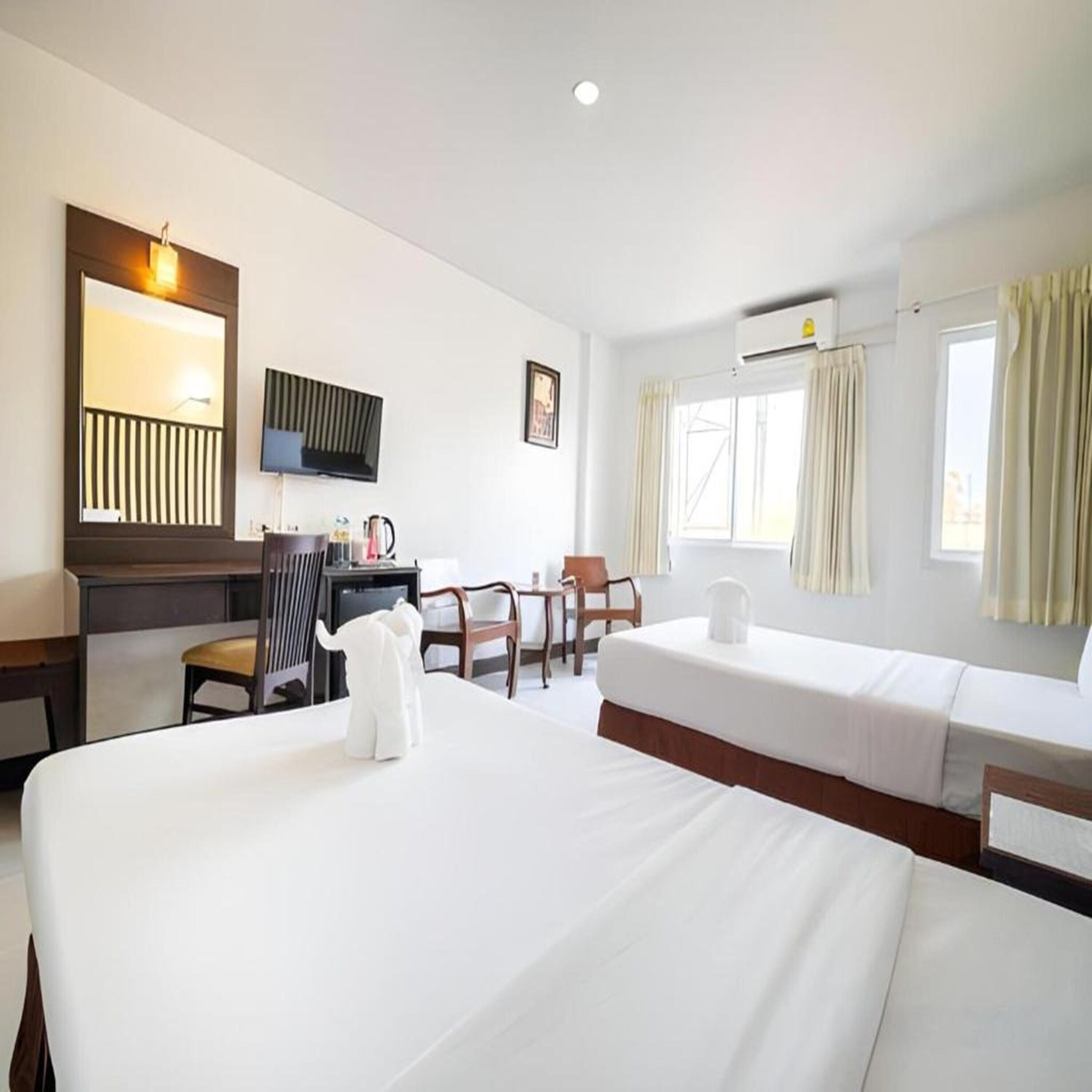 A hotel room with two beds, a desk with a chair, a television, and a window with curtains.