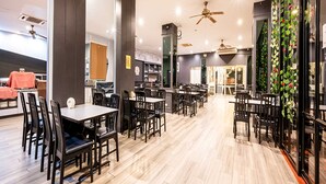 Un vaste espace dédié à la salle à manger, avec de nombreuses tables et chaises, des ventilateurs de plafond et un aménagement intérieur moderne.