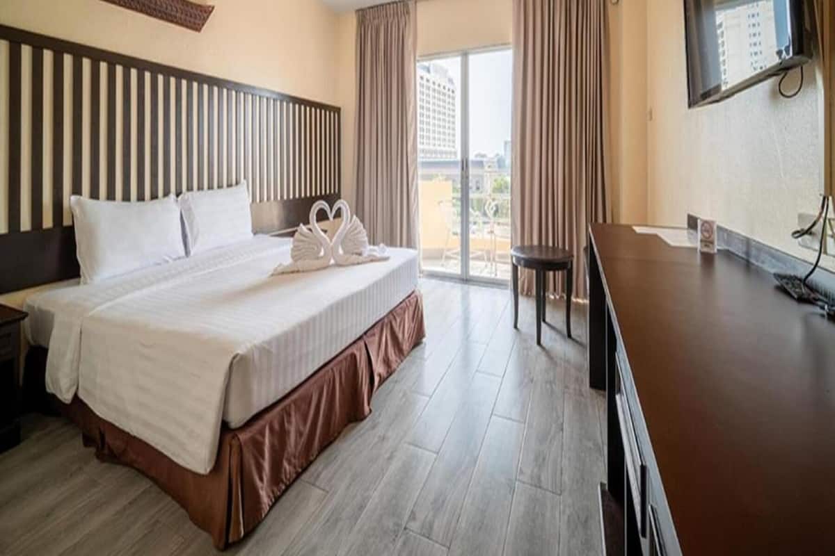 Een hotelkamer met een groot bed, een bureau, een stoel, een televisie en uitzicht op gebouwen.