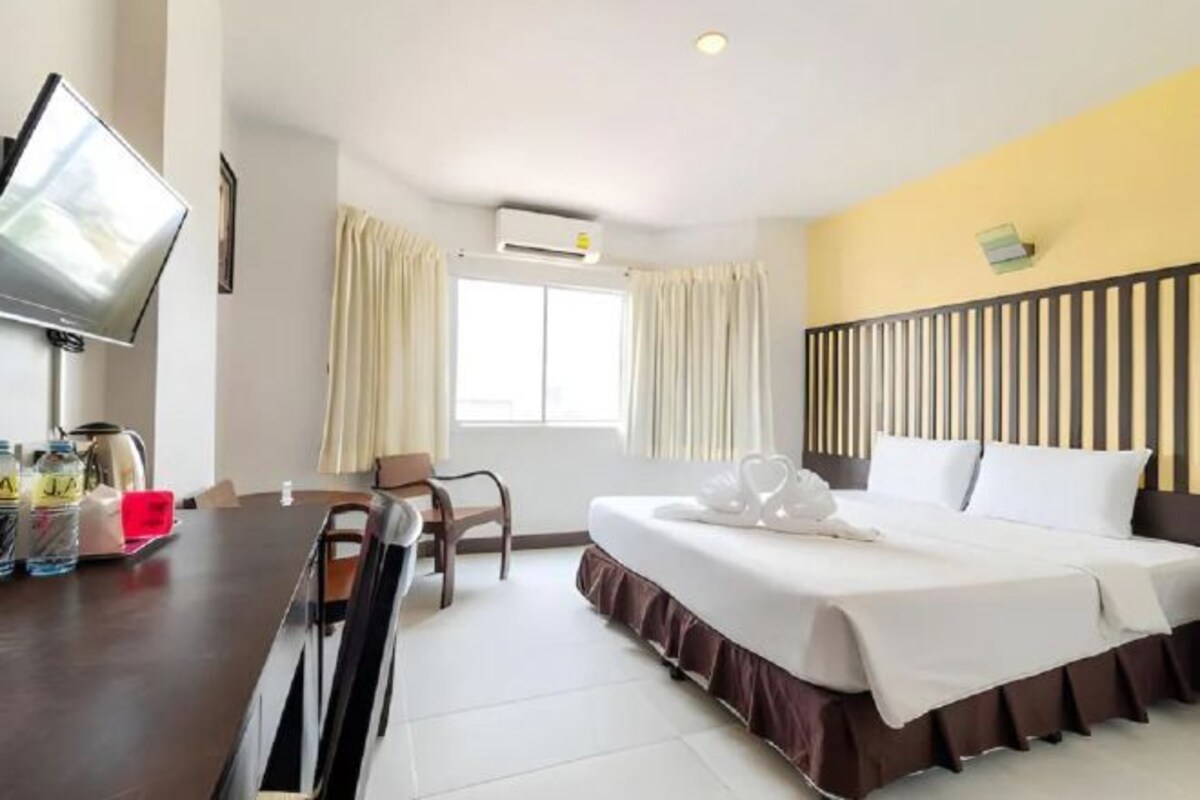Een hotelkamer met een bed, een televisie, een bureau met stoel, een raam met gordijnen en een airconditioning.