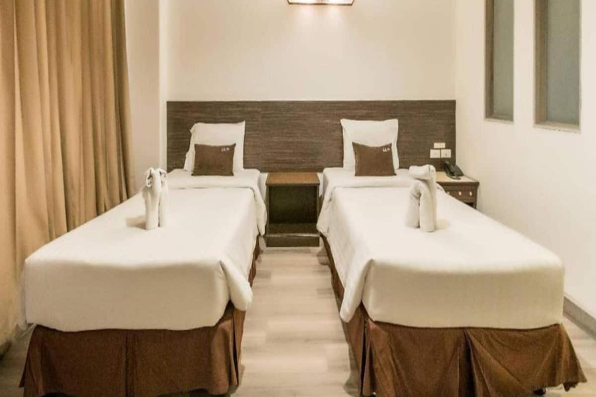 Een hotelkamer met twee bedden, een houten hoofdbord, een nachtkastje, een lamp en een raam.