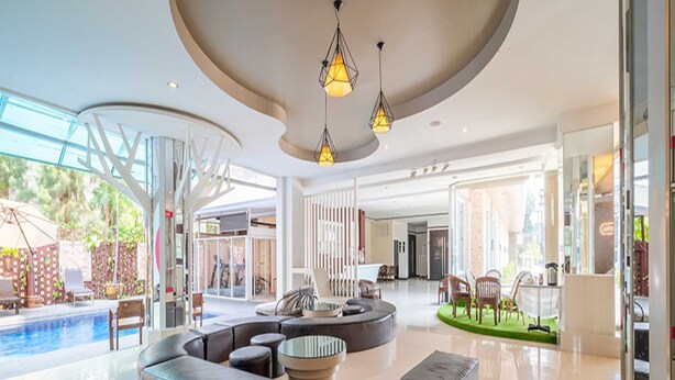 Un hall d’entrée spacieux avec un espace salon aux lignes courbes, une piscine et un espace extérieur clos par des parois de verre.