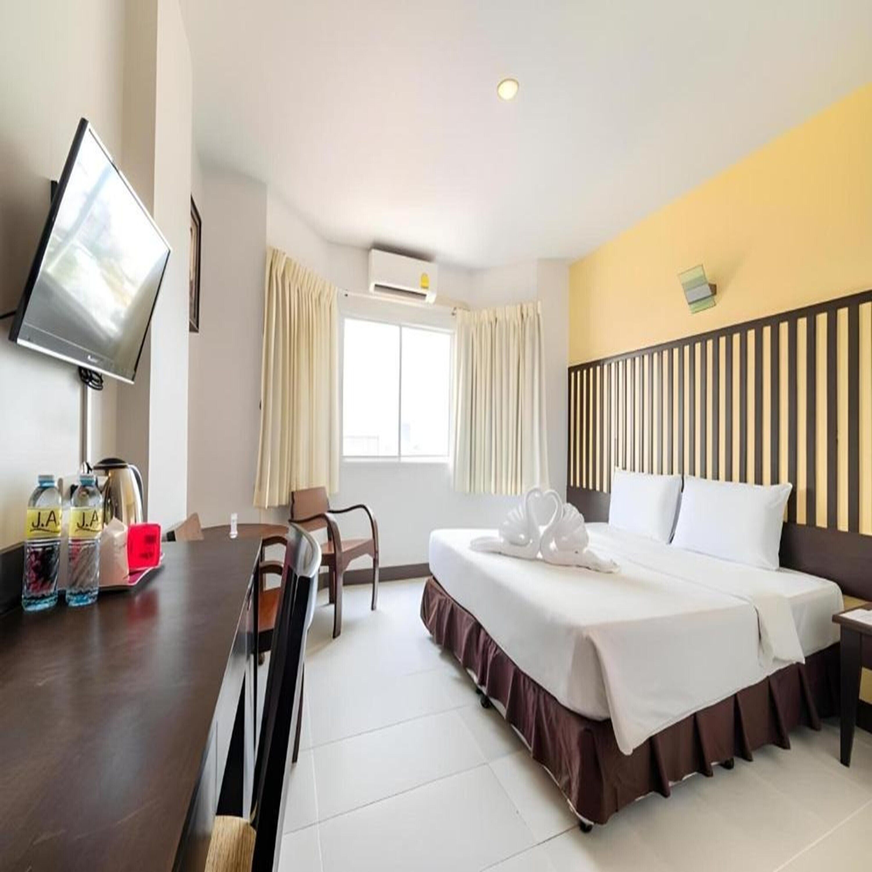A hotel room with a bed, a desk with a chair, a television, and a window with curtains.