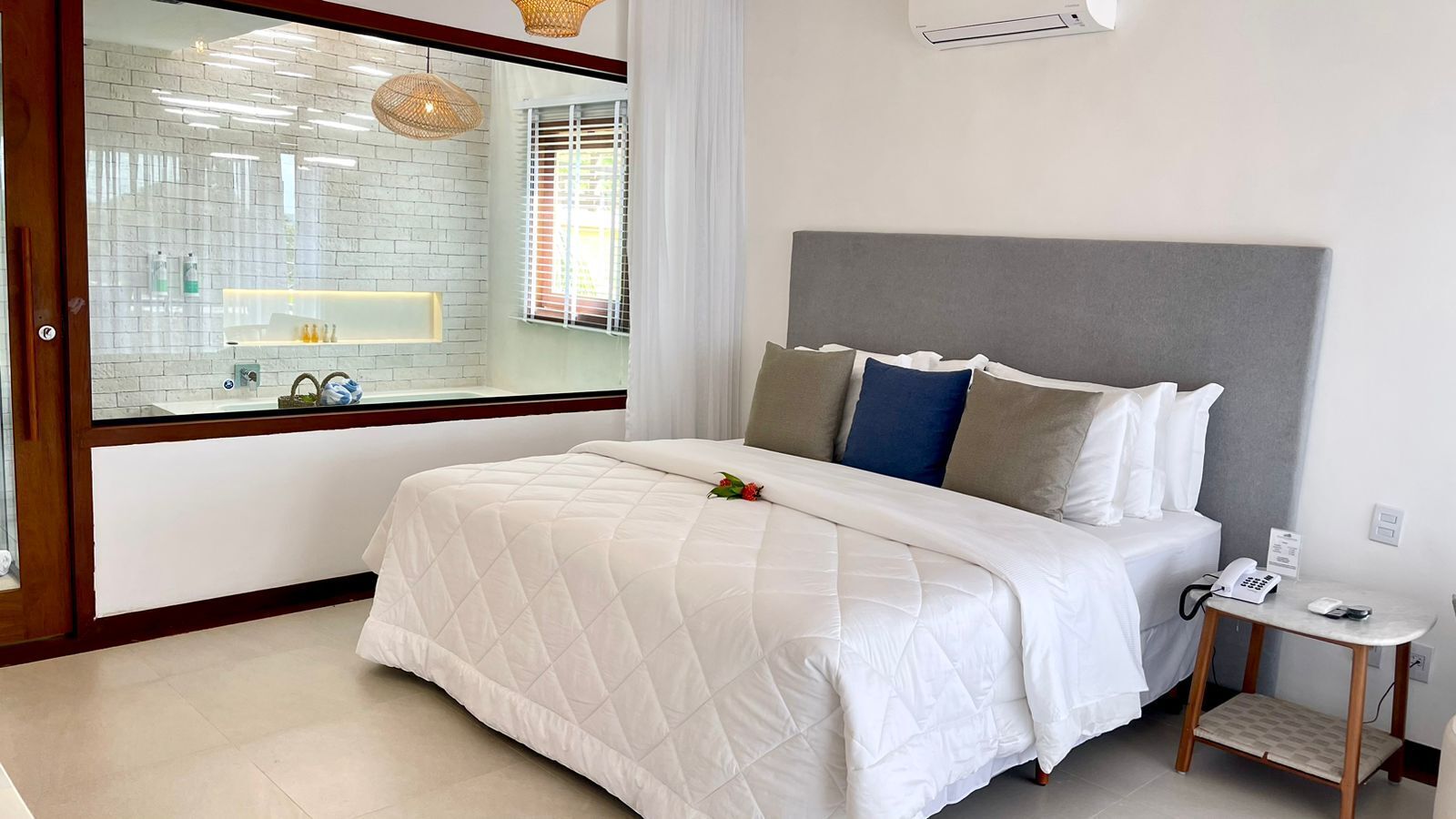 A modern hotel room with a large bed, a bedside table with a phone, and a view of a bathroom with a mirror and sink.