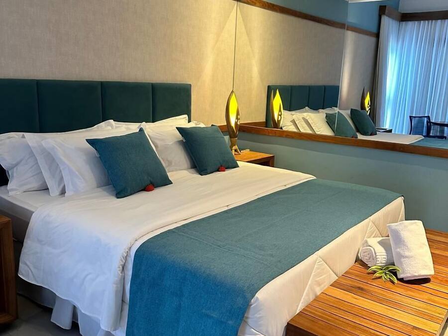 A hotel room with a large bed, a wooden nightstand, a bedside table with a towel, and a mirror reflecting the room.