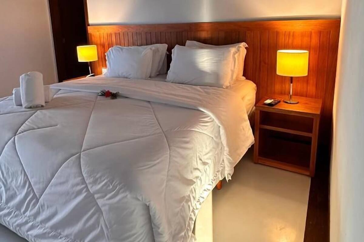 Ett hotellrum med en stor säng, två sängbord med lampor och ett träpanelat tak.